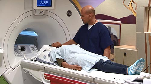 Radiólogo preparando a un paciente para un examen por resonancia magnética nuclear (RMN).
