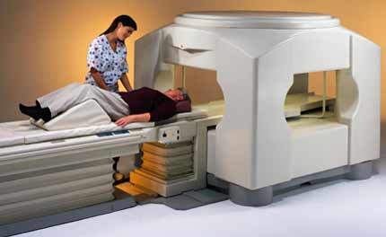 An open MRI unit. A technologist is shown attending a patient lying on the gantry